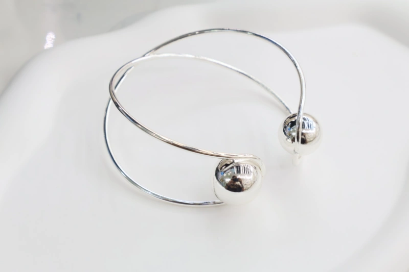 Silver double ball crossover cuff bracelet with polished metal finish, crossed wire open bangle structure and round ball end details for wholesale jewelry buyers