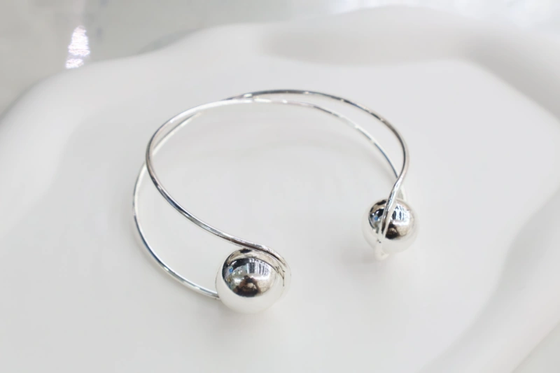 Silver double ball open cuff bracelet with polished metal finish, crossed wire bangle structure and round ball end details for wholesale jewelry buyers