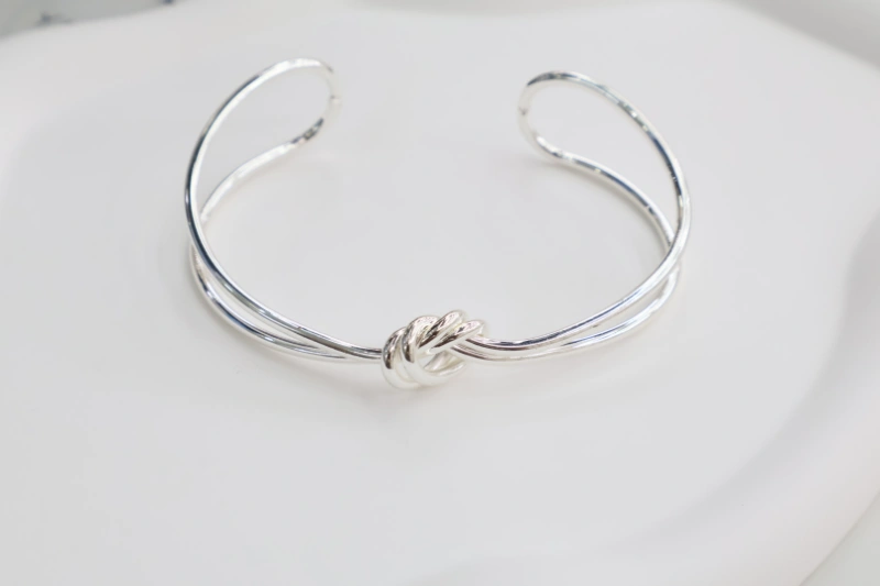 Silver knot open cuff bracelet with polished metal finish, double line bangle structure and central knot design for wholesale jewelry buyers