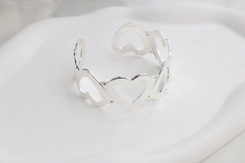 Silver open heart cuff bracelet with connected hollow heart shapes, polished metal finish and romantic open bangle design for wholesale jewelry buyers
