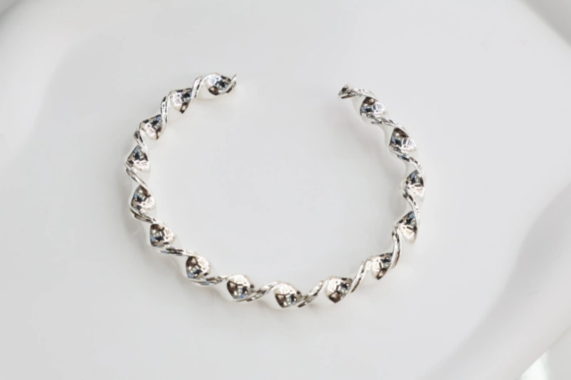 Silver twisted open cuff bracelet with polished metal finish, braided wave-like texture and modern statement bangle design for wholesale jewelry buyers