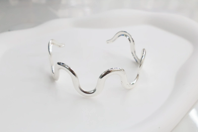Silver wave open cuff bracelet with polished metal finish, abstract wavy line design and minimalist open bangle structure for wholesale jewelry buyers