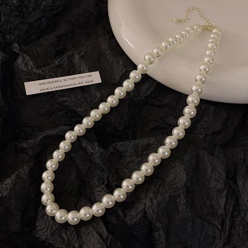 Classic white pearl strand necklace with adjustable gold-tone extension chain on black textured background for wholesale jewelry buyers