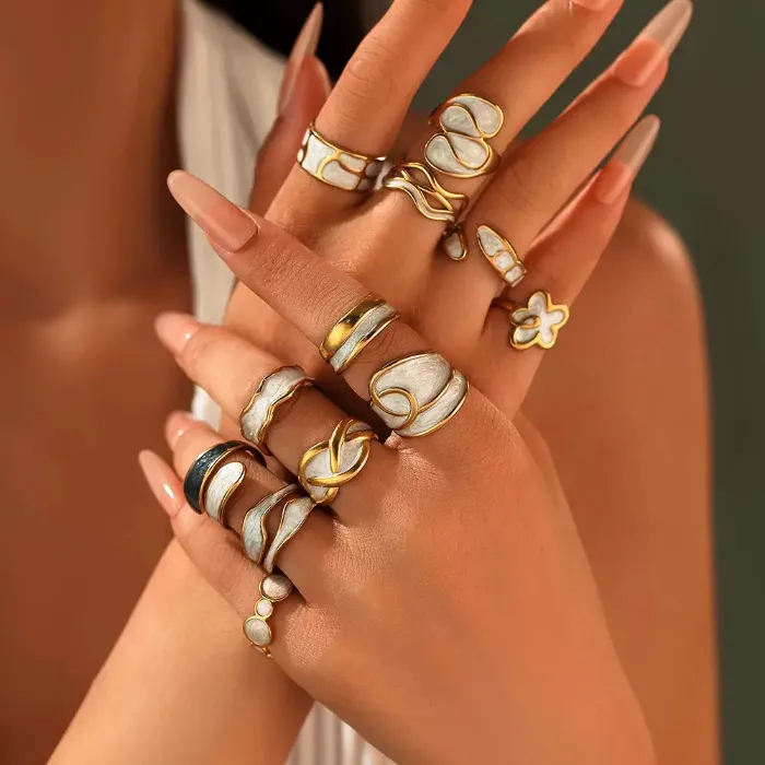 Gold white shell statement rings set with abstract, flower, wave and textured ring designs shown on hand for wholesale jewelry buyers